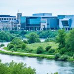 University of Alberta campus buildings overlooking the North Saskatchewan River valley with pedestrians on a riverside walkway.